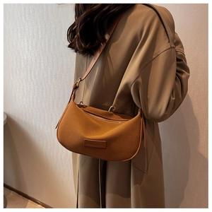 Close-up of a brown suede crescent bag with adjustable strap worn on a beige trench coat