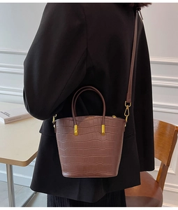 Detailed view of brown crocodile texture leather and gold metal buckle on bucket bag