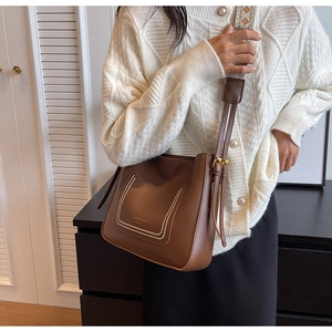 Detail of brown leather bucket bag with gold rivets and ethnic style woven strap