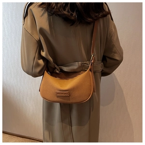 Close-up of caramel suede crossbody bag with premium leather logo tag and bronze zipper