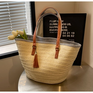 Close-up of a straw tote bag with brown leather handles and a decorative tassel charm