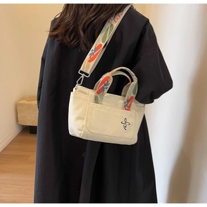 Detail of canvas tote bag featuring floral embroidery and colorful patterned strap design