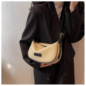 Detail of beige crescent crossbody bag with black leather piping on a model