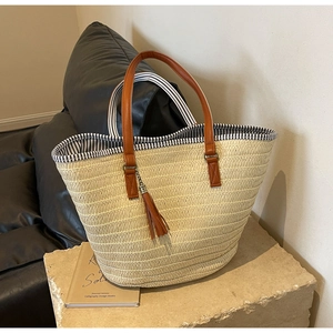 Detail of straw tote bag featuring brown leather handles and a decorative tassel accent