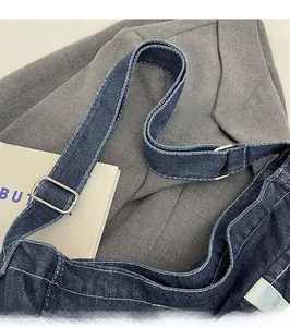 Detail of the adjustable shoulder strap on a navy denim messenger bag with white stitching