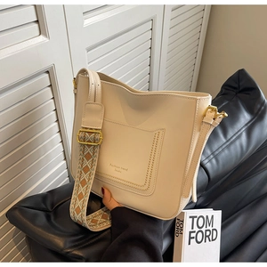 Detail of cream bucket bag featuring ethnic embroidered wide strap and golden hardware