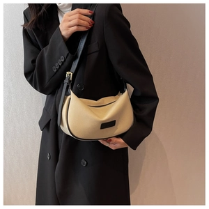 Detail of beige half-moon bag with black leather trim and adjustable shoulder strap