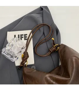 Detail of a brown leather hobo bag with a knotted shoulder strap and gold metal hardware