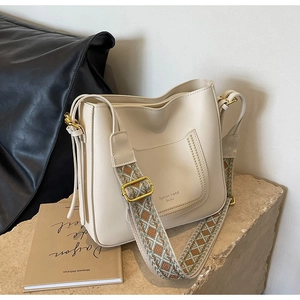 Close-up of cream bucket bag with wide geometric strap on stone texture display