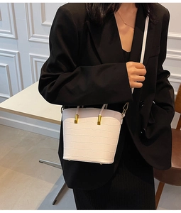 White crocodile pattern bucket bag with gold hardware shown as a crossbody on a model