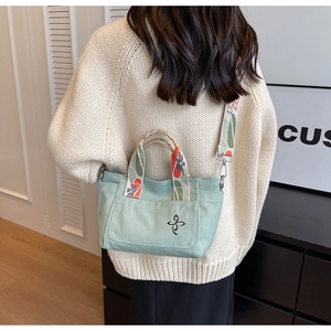 Detail of light green canvas tote bag featuring floral embroidery and patterned shoulder strap