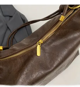 Close-up of smooth gold metal zipper on brown textured leather shoulder bag for women