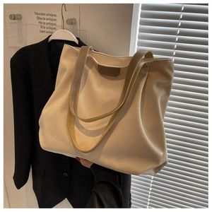 Detail of a large beige canvas tote bag with khaki leather straps and brown logo patch