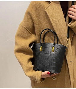 Detail view of black crocodile pattern bucket bag with gold hardware on a wool coat
