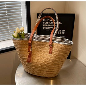Detail of handmade straw tote featuring leather handles, tassel accent, and striped lining