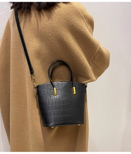 Detail of black faux crocodile leather bucket bag with gold hardware on camel coat