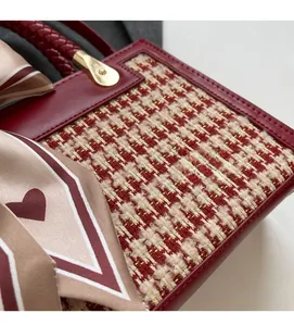 Detail of red tweed handbag featuring gold hardware and elegant silk scarf accessory