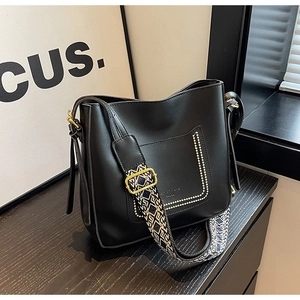 Detail of black leather bucket bag featuring white geometric wide strap and gold hardware