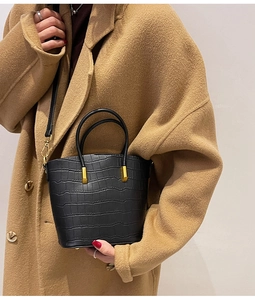 Detail of black crocodile texture bucket bag with gold hardware on camel wool coat