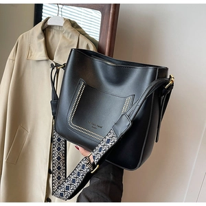 Detail of black leather bucket bag with decorative pocket and stylish embroidery strap