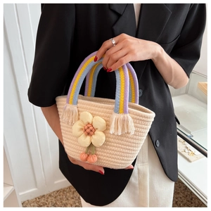 Détail d'un sac seau tissé beige avec fleur en tissu jaune et anse rayée multicolore