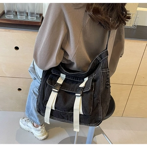 Side view of large black denim messenger bag with white buckles worn by a model