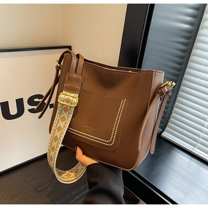 Close-up of brown leather bucket bag featuring white contrast stitching and woven strap