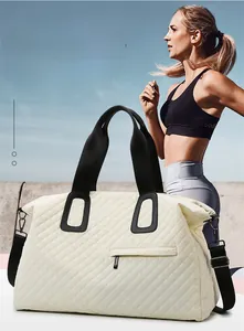 Quilted beige duffle bag with black straps worn by a model against a clear blue sky