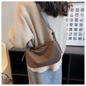 Brown leather crescent shoulder bag styled with a beige knit sweater and grey skirt