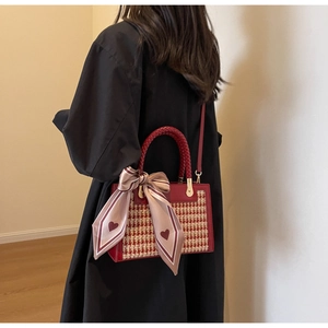 Detail view of red houndstooth square handbag with woven handle and silk scarf