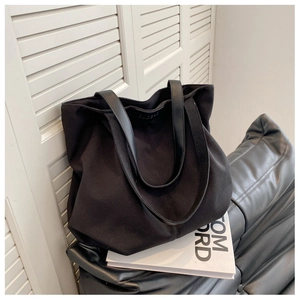 Close-up of black canvas tote bag showing the embossed logo and leather handle