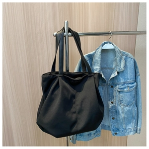 Close-up of a black canvas tote bag with soft texture hanging against a denim jacket