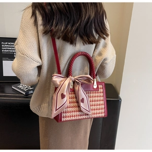 Close-up of houndstooth crossbody bag with red woven handle and pink silk bow detail