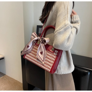 Close-up of red houndstooth handbag with woven handle and pink heart silk bow detail