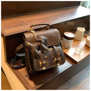 Détail d'un sac à dos rétro marron foncé avec motifs d'ours et charm ours en peluche