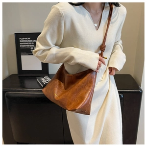 Detail of vintage brown leather bag showing knotted strap and gold lettering on white dress