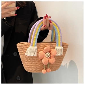 Dettaglio dei manici arcobaleno e del grande fiore in tessuto su borsa in paglia intrecciata
