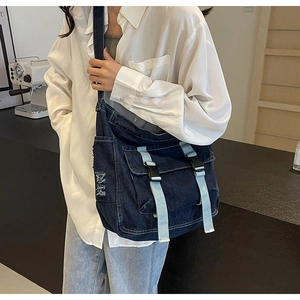 Détail d'un sac messager en denim bleu avec poches avant à rabat et boucles de fermeture