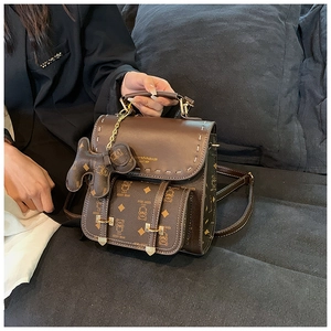 Détail d'un sac à dos en cuir marron foncé avec motifs vintage et charme d'ours