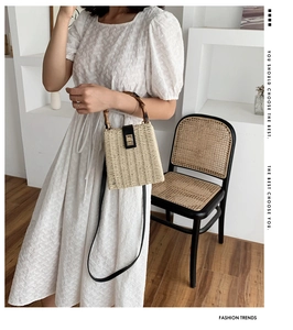 Detail of handwoven straw handbag with bamboo handle and black leather strap worn with white dress