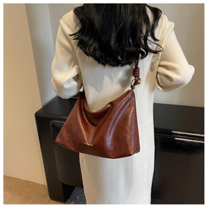 Detail of caramel leather shoulder bag with gold text and unique knotted strap design
