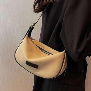 Chic beige crescent shoulder bag with black trim and adjustable strap shown on model
