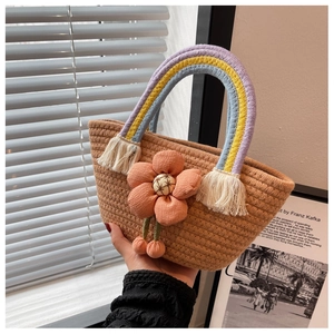Dettaglio della borsa in paglia con manico color arcobaleno e ciondolo a fiore in tessuto arancione