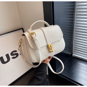 Detail of white litchi leather texture and golden metal twist lock on a small square bag