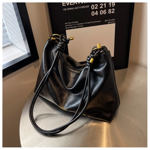 Detail of black faux leather tote featuring knotted shoulder strap and gold hardware