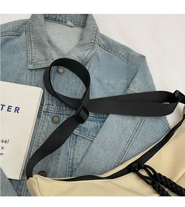 Detail of smooth nylon crescent bag with adjustable black strap on denim jacket