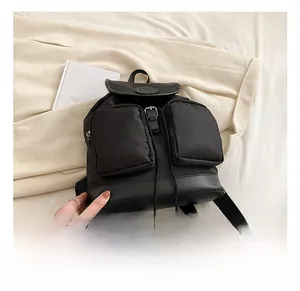 Detail of black nylon backpack with dual front pockets and drawstring closure on soft bedding