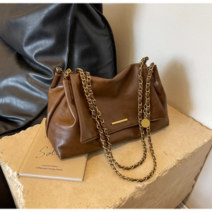 Détail d'un sac vintage en cuir marron foncé avec chaînes dorées sur plateau en pierre