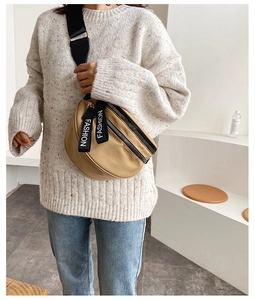 Detail of beige nylon crossbody bag with black zippers and FASHION logo strap
