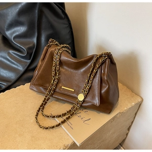 Détail de la texture en cuir marron foncé avec bandoulière chaîne dorée et métal chic